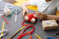 A boy wrapping up a present with a red ribbon. 