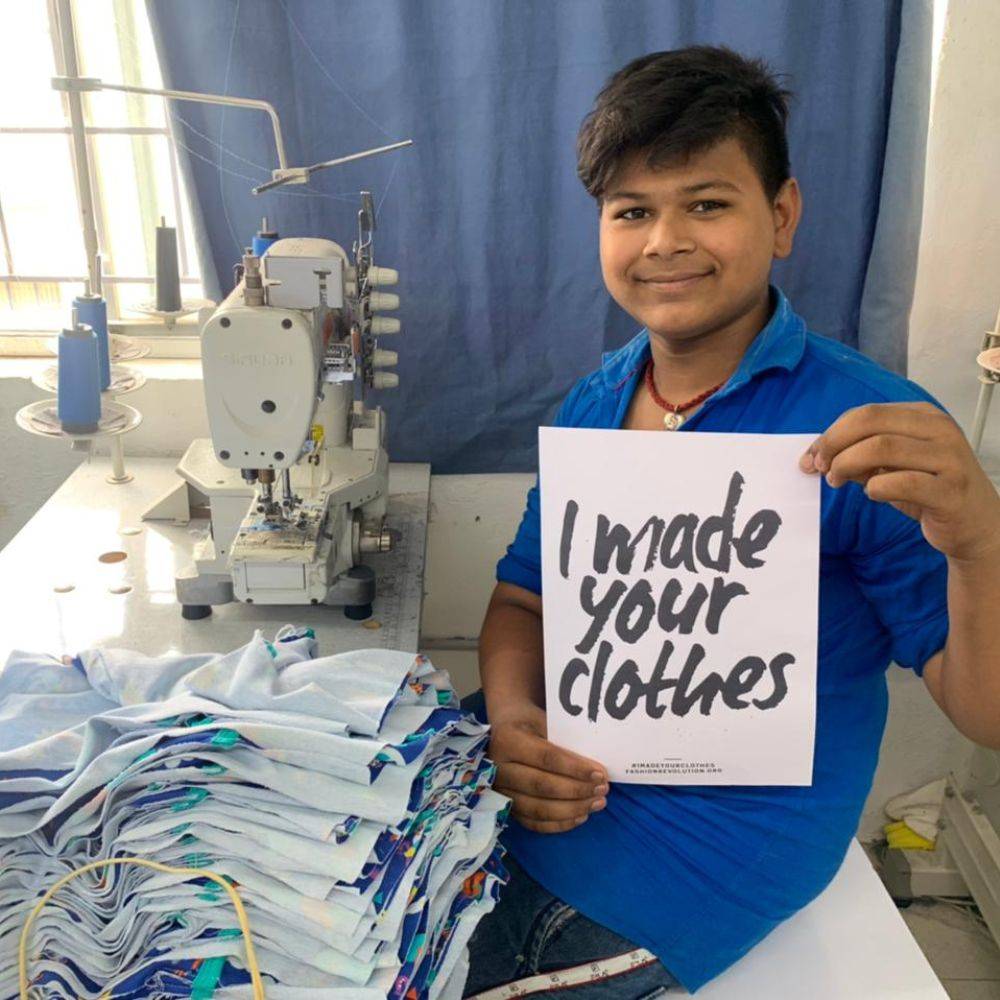 Image of a smiling man in a textile factory holding a sign that says 'I made your clothes'