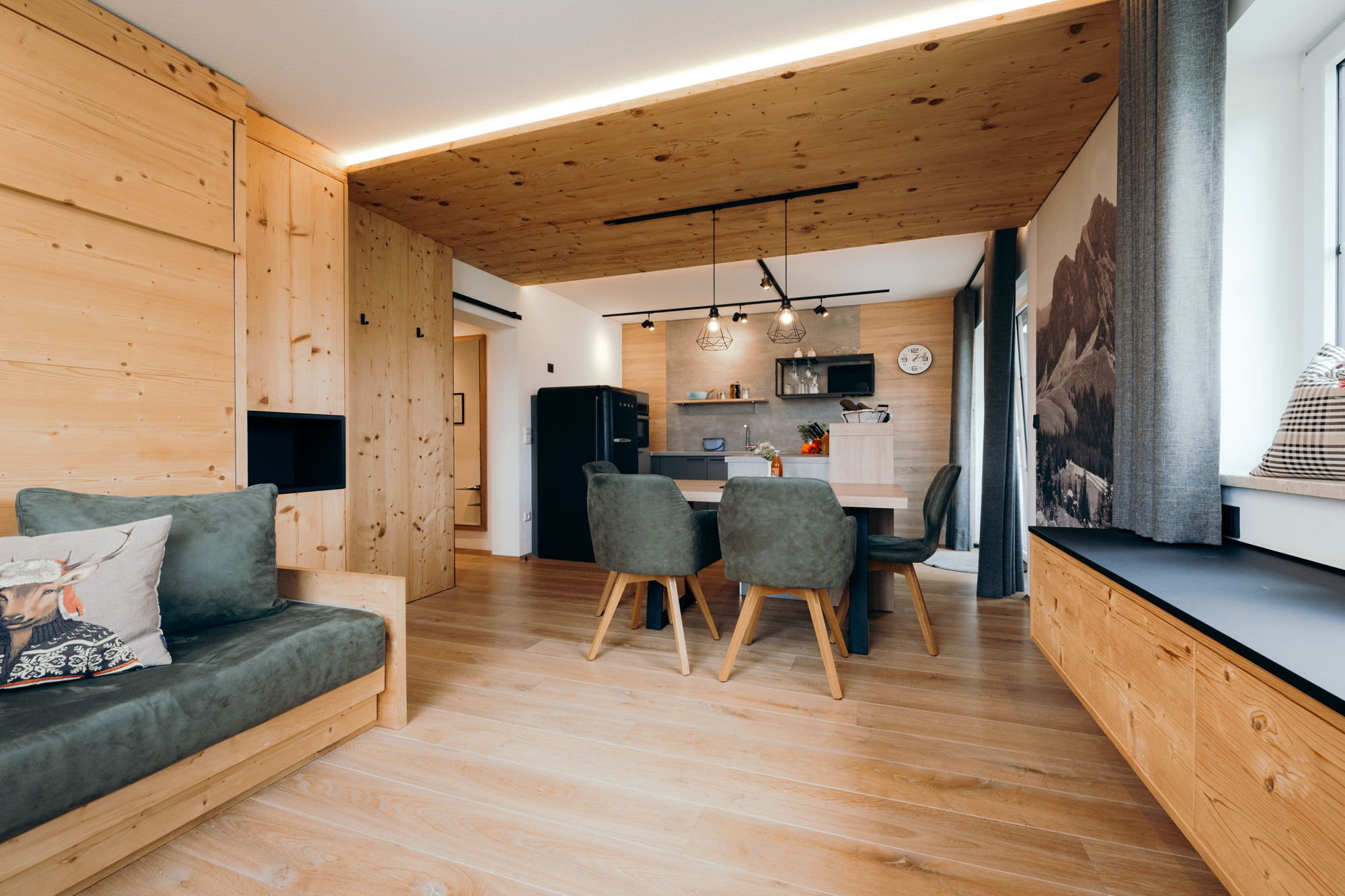 Ein mit hellem Holz verkleidetes Wohnzimmer, im Hintergrund eine moderne Küche mit Esstisch.
