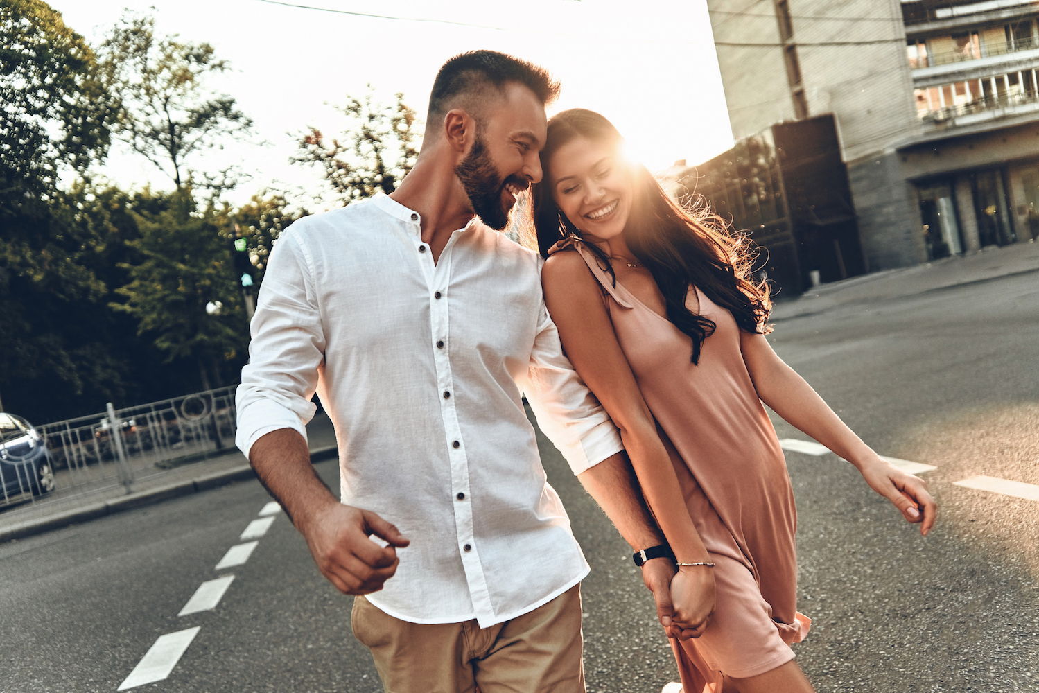 An attractive latin couple wearing comfortable summer clothing walk on a sidewalk smiling to eachother.