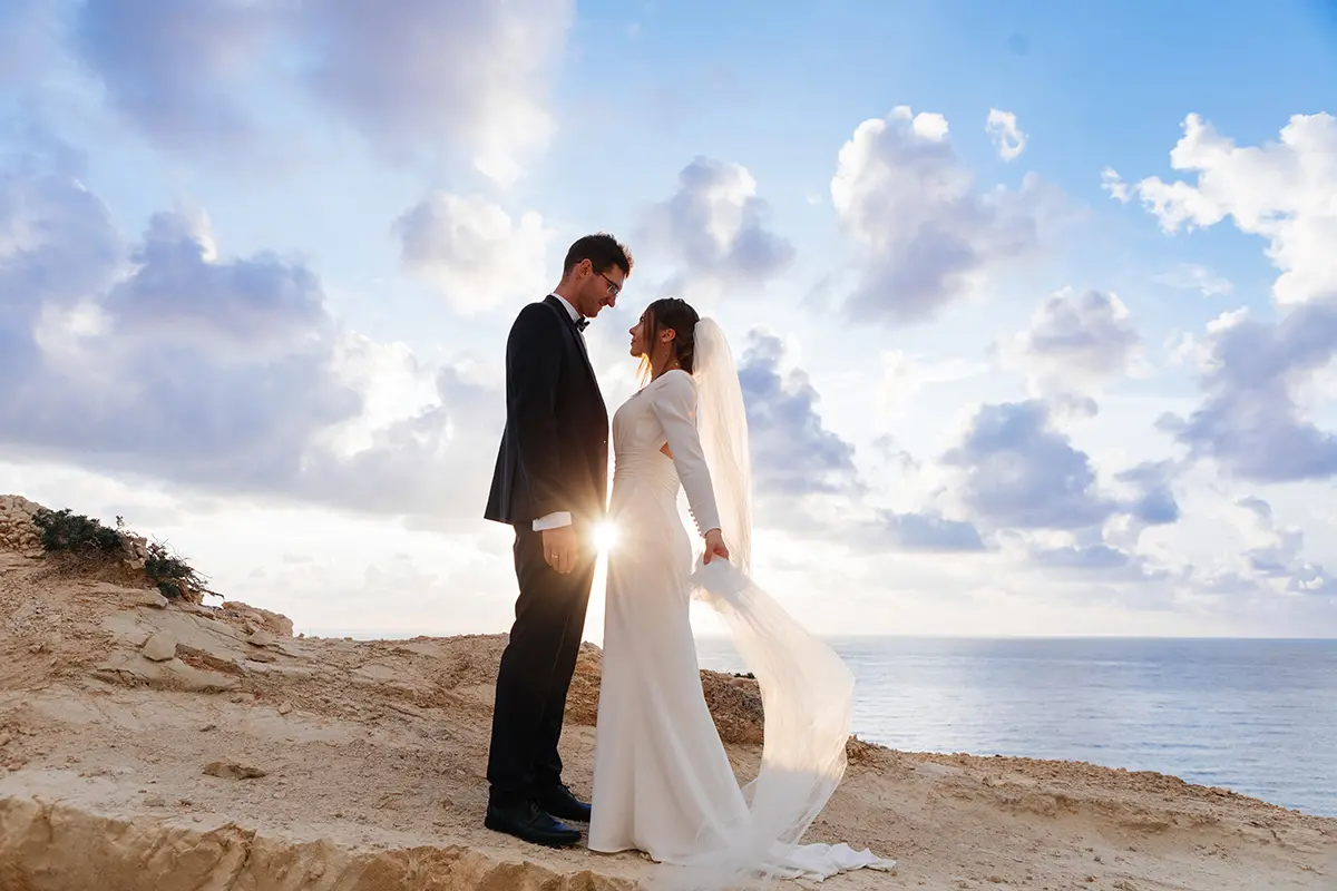 Une photo de la mariée et du marié debout sur des rochers surplombant une belle plage rocheuse à Paphos.