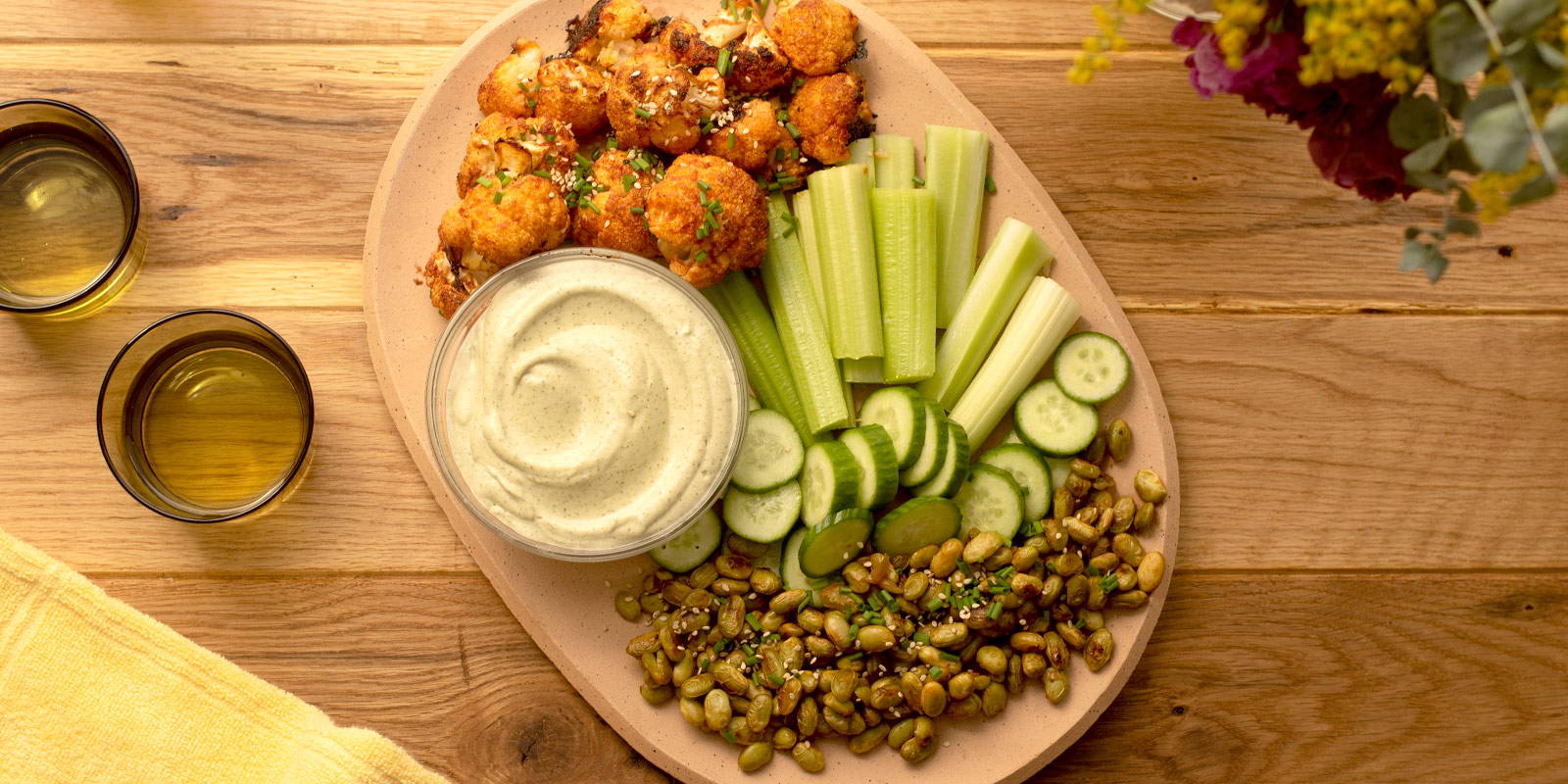 Wooden platter with cauliflower wings, edamame, cashew ranch, celery, and cucumbers.