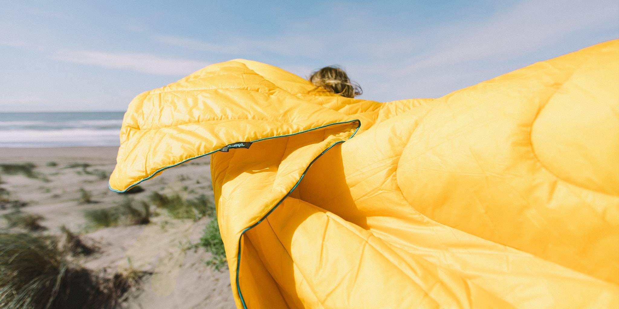 Woman standing on a sandy beach with a yellow Rumpl outdoor blanket
