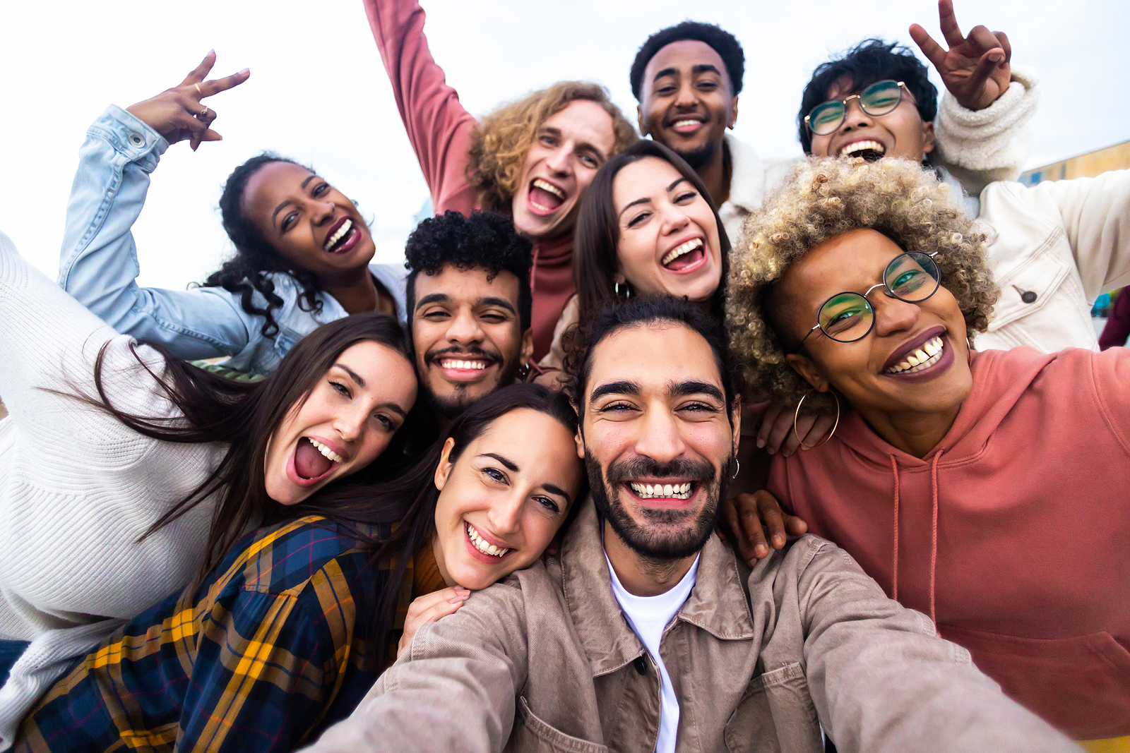 A large group of friends smile and laugh as they pose for a picture holding peace signs.