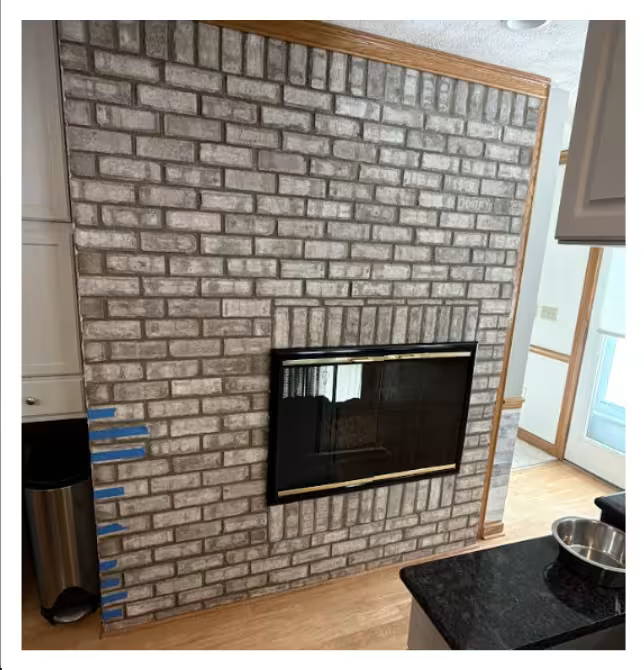 Interior brick fireplace wall with a built-in firebox insert, showing clean, evenly spaced brickwork and surrounding wood trim.