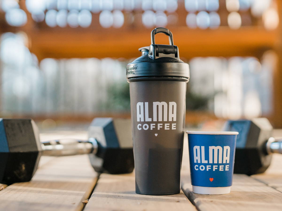 Blender bottle and cup of coffee beside weights