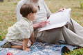 Young child sitting outdoors with an older adult while looking through a book together during shared reading time