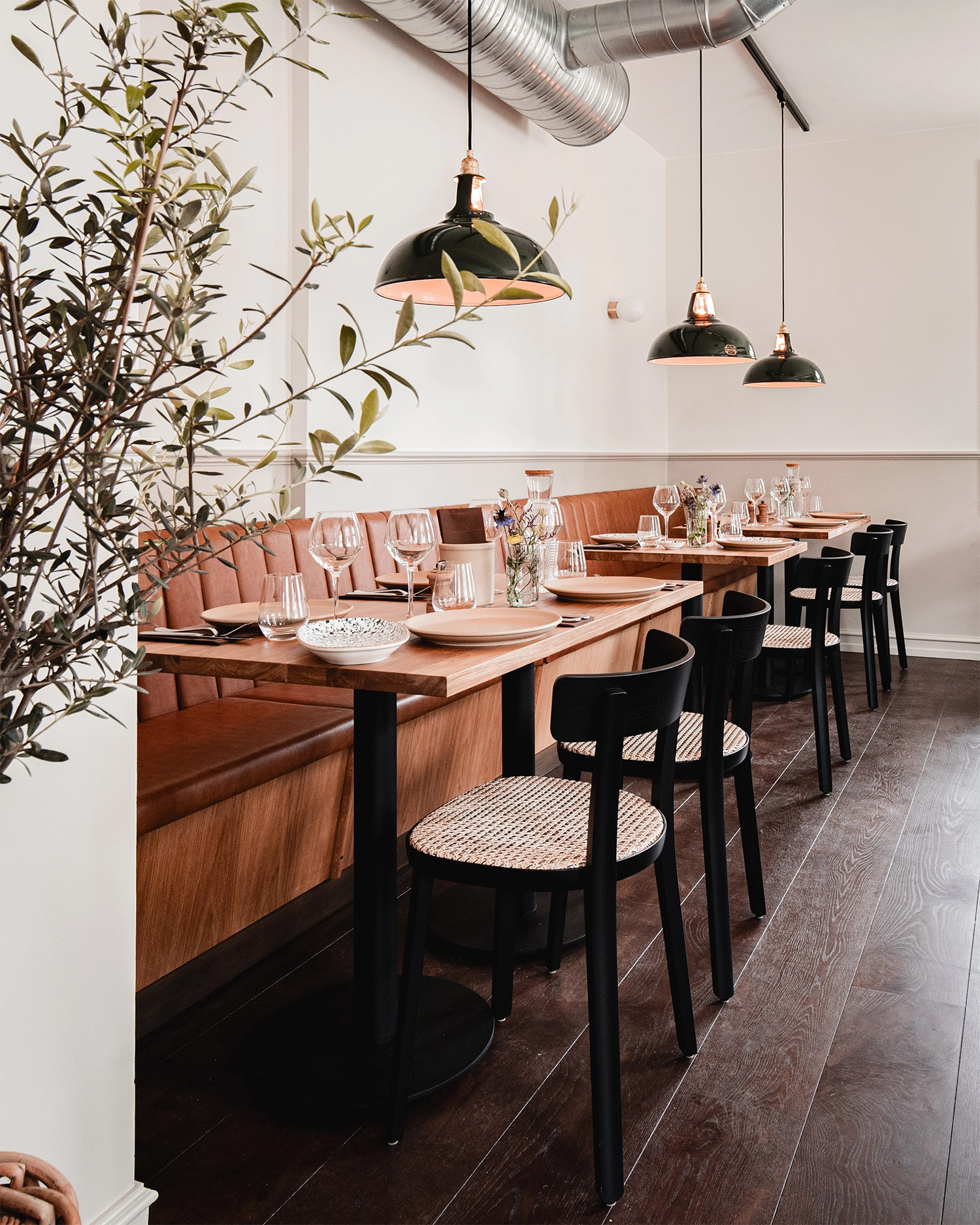 Three large green Coolicon Lampshades hanging over wooden nordic restaurant tables and chairs with white walls. 