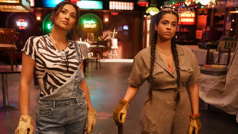 Stella and Viv standing confidently at the bar. Viv is holding a bat on one hand.