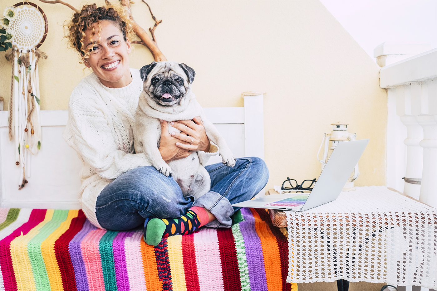 girl sits on bed with pug dog and laptop