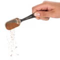 A hand pours a brownish ground spice out of a metal tablespoon