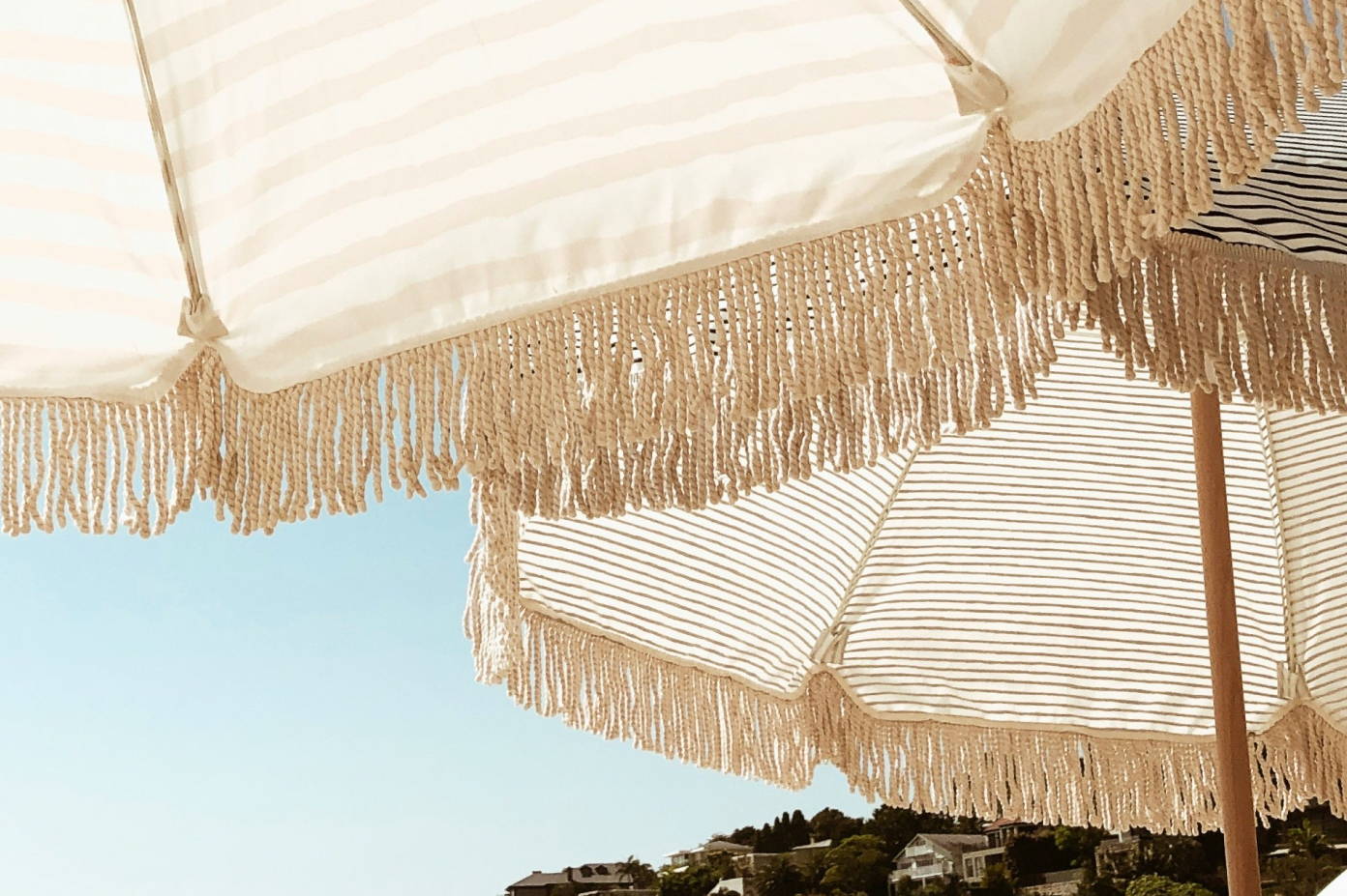 A pair of tan umbrellas at the beach with blue skies.