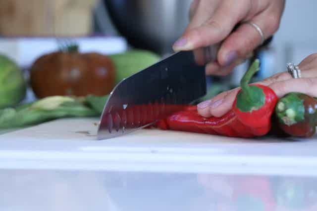 Close-up of hands slicing fresh red chili peppers on a white cutting board in a kitchen setting.