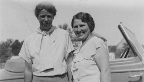 Eleanor and Lorena standing close in front of a car. They are both smiling at the camera, Lorena more serious.