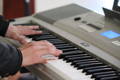 An image showing hands pressing the keys of an electric keyboard. 