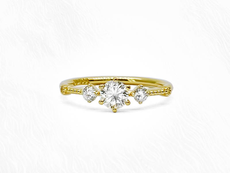 Yellow gold engagement ring with central round diamond and two small side diamonds.