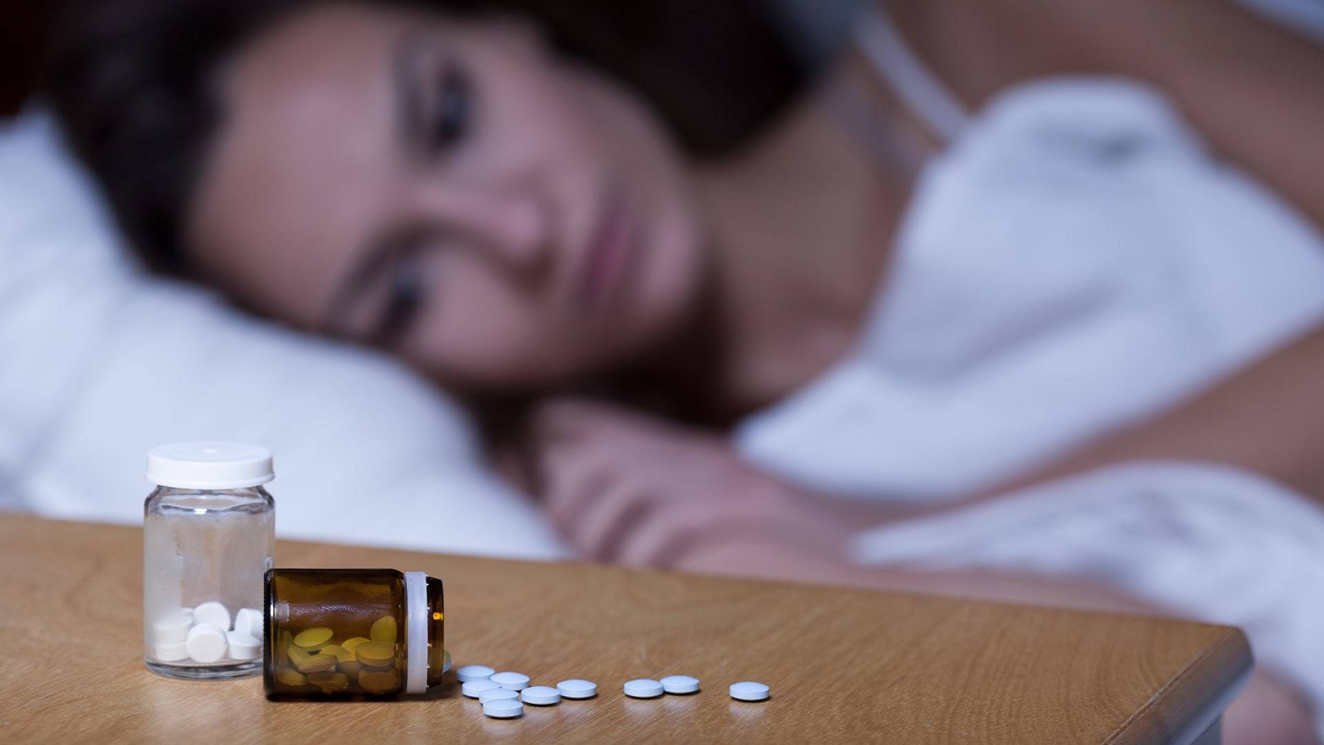 Woman unable to sleep, with melatonin pills on the nightstand