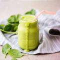 Mason jar overfilled with a super green powder smoothie with spinach surrounding the glass.