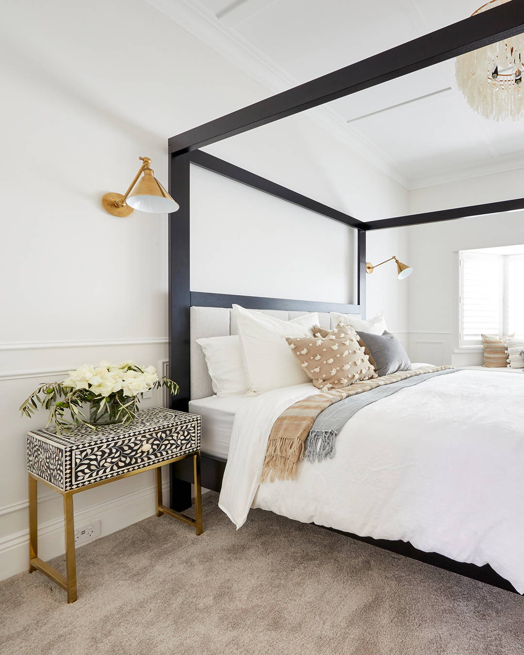 A bedroom setting with a four poster bed, lush white linens and fresh flowers on the bedside 