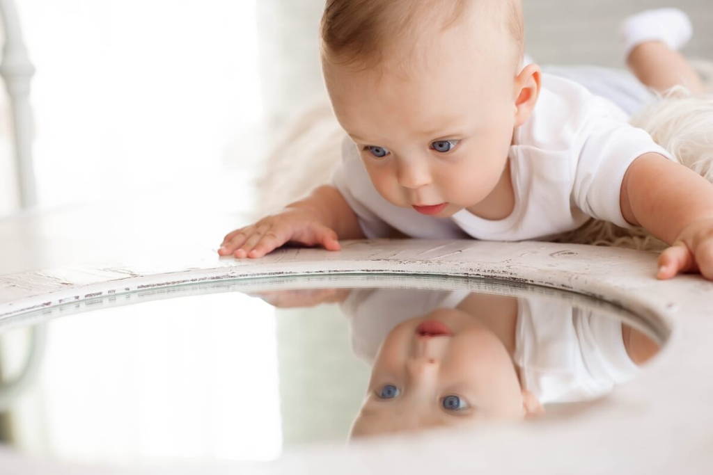 Baby lying on its belly and looking at a round mirror.