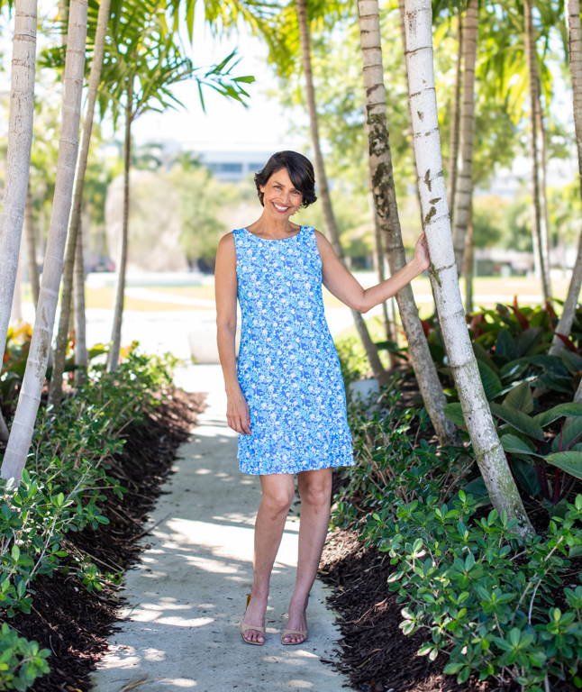 A woman wears a blue dress next to palm trees.