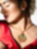 A woman in a red blouse wears a gold necklace with a green fan-shaped pendant, her hair adorned with flowers, shown against a bright background.