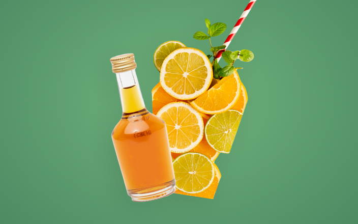 A bottle of alcohol and slices of oranges and lemons arranged in the shape of a glass with a straw and sprig of herbs for Confetti's Virtual Cocktail Kit
