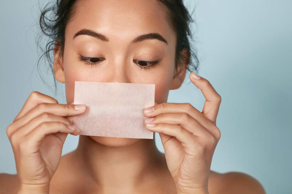 woman blotting her oily nose and skin with blotting paper