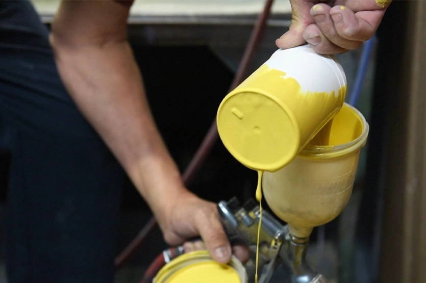 A person pouring yellow liquid vitreous enamel into a spray gun