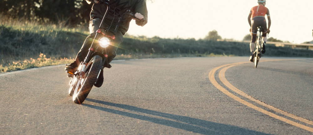 a man riding a SUPER73 electric mini moto with and a road biker riding the other direction