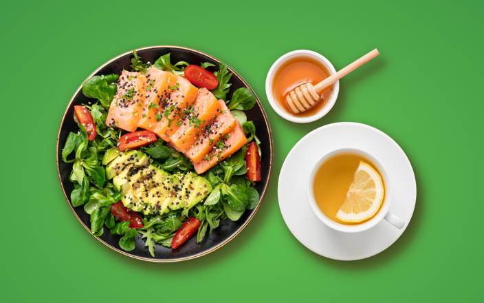 A salad with avocado and salmon next to a cup of green tea and a bowl of honey for Confetti's Virtual Nutrition Class