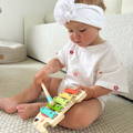 Little girl sitting and playing on a colorful wooden xylophone featured in the Montessori Music Set.