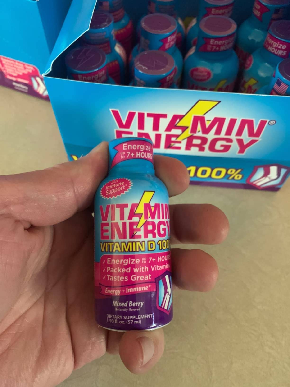 A hand holding a bottle of Vitamin Energy dietary supplement.