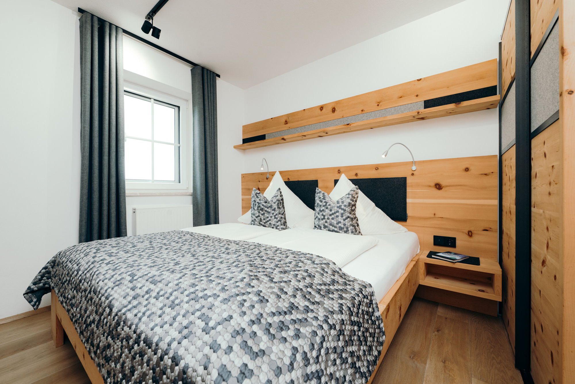 Ein weiß bezogenes Bett mit mehrstufig grauem Überzug in einem modernen Schlafzimmer.