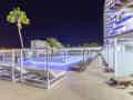 Beleuchteter Außenpool bei Nacht mit Liegestühlen und privaten Cabanas vor dem Hotelgebäude.