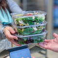 People exchaging a stack of 3 different salads in stackable food packaging