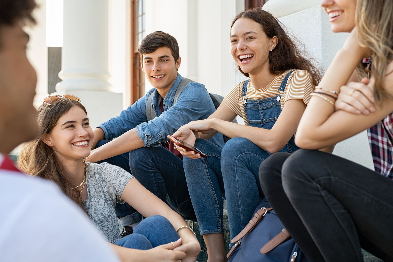 A group of young adults talk in a group focusing on one girl in particular, smiling and laughing together.