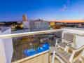 Balkon mit Sitzgelegenheiten und Blick auf den beleuchteten Pool sowie die Stadt bei Sonnenuntergang.