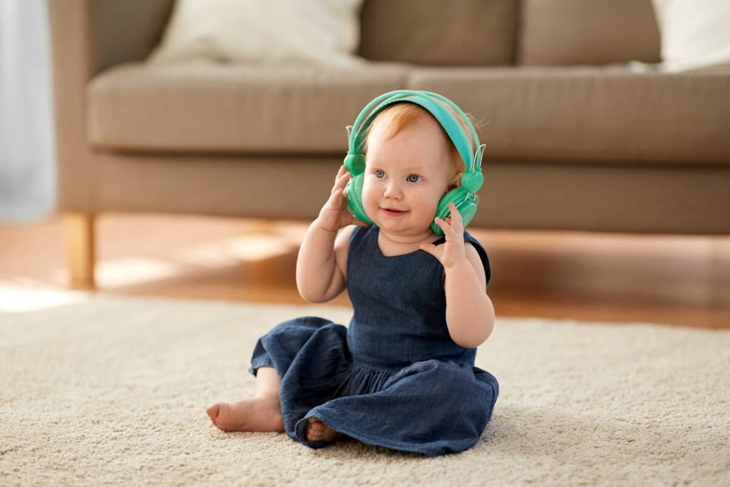 Baby sitting on a carpet and listening to a song on green headphones.