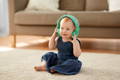 Baby sitting on a carpet and listening to a song on green headphones.