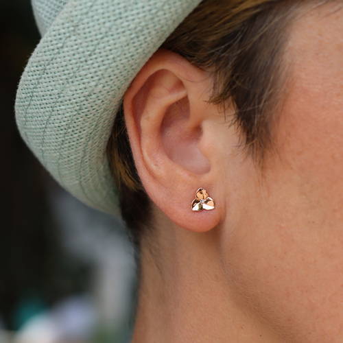 Boucle d'oreille fleur à trois pétales style bouton en or rose avec petit diamant au centre portée par une femme.