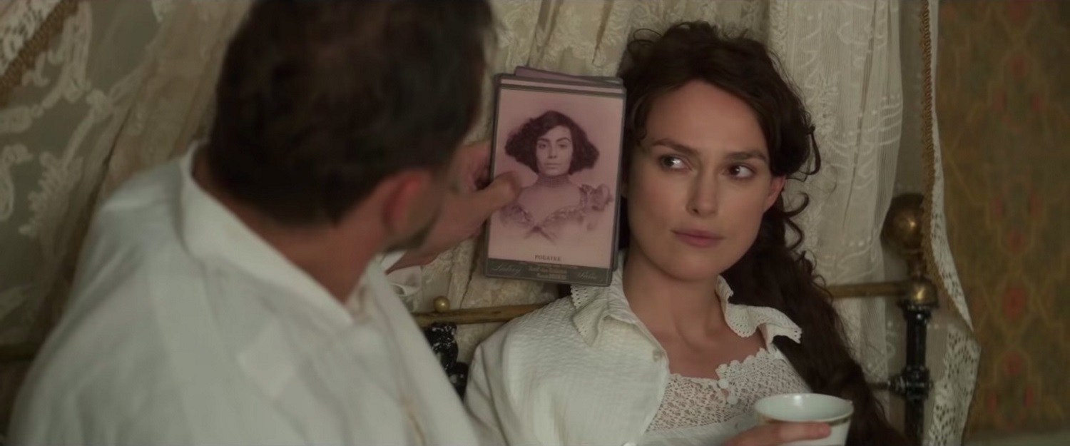 Willy holds a drawing of Colette next to her face. Colette looks over at him smiling.