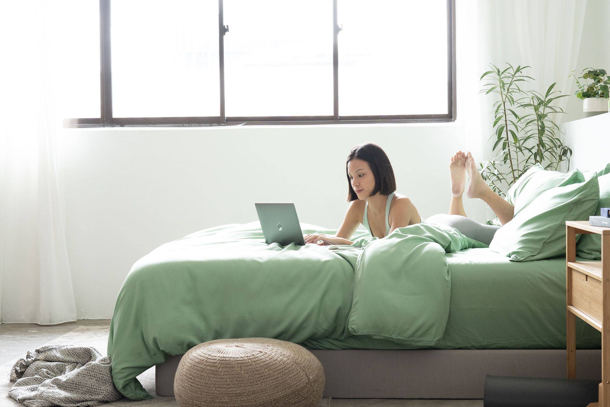 Girl using laptop on bed featuring Weavve’s tencel Lyocell Classic Set in green colour