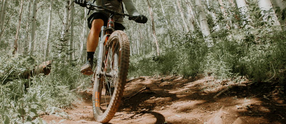 the front wheel of a mountain bike, with a man riding on a trail in the forest