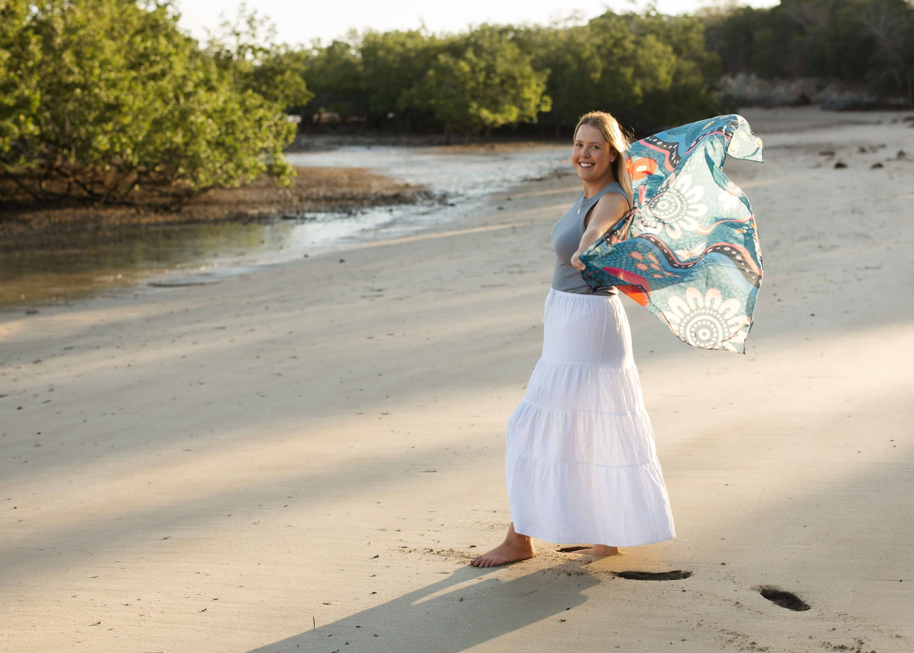 Caitlin holding a scarf with her artwork on the beach next to a river