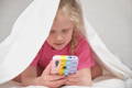 Toddler using smartphone under blanket during quiet time at home.