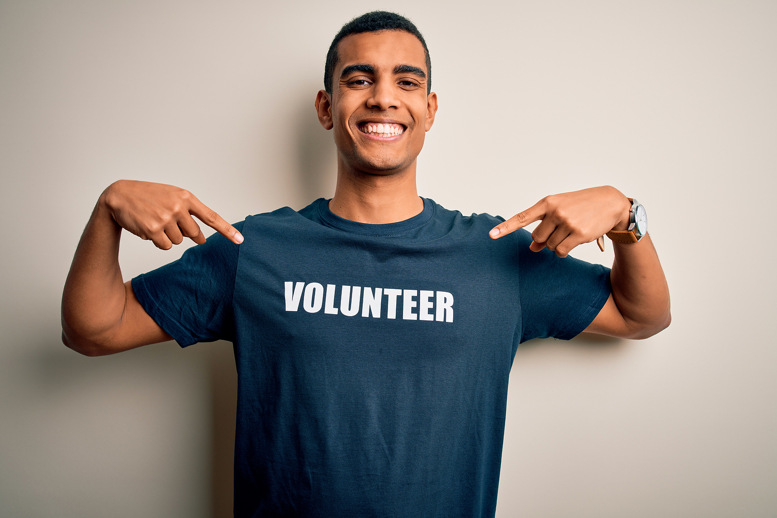 Young handsome African American man volunteering wearing t-shirt with volunteer message looking confident with smile on face, pointing oneself with fingers proud and happy.