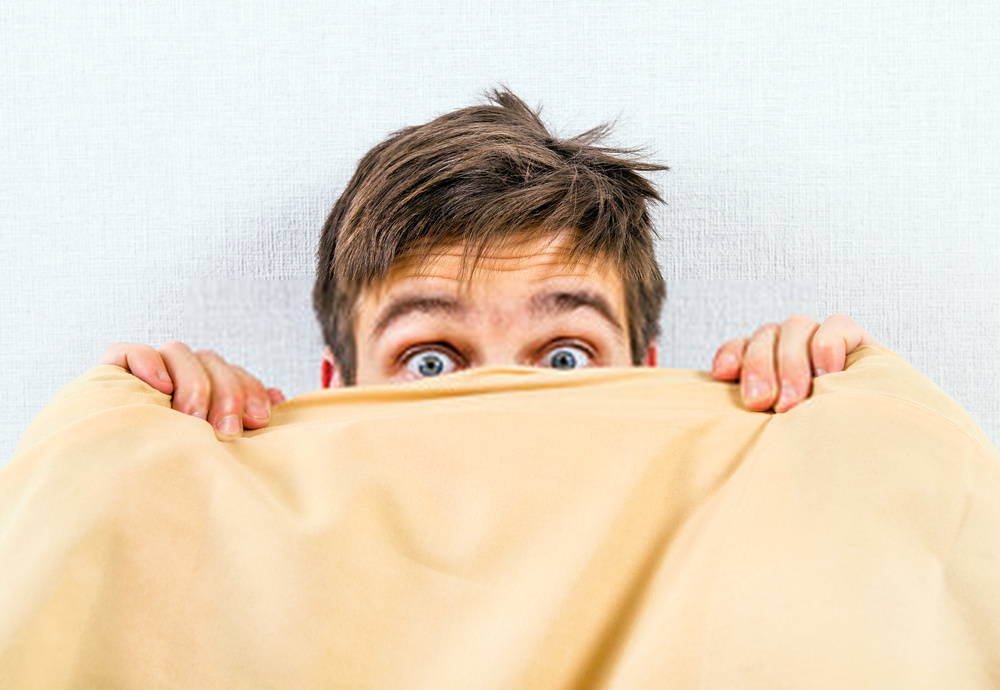 Young man with blue eyes hiding under covers