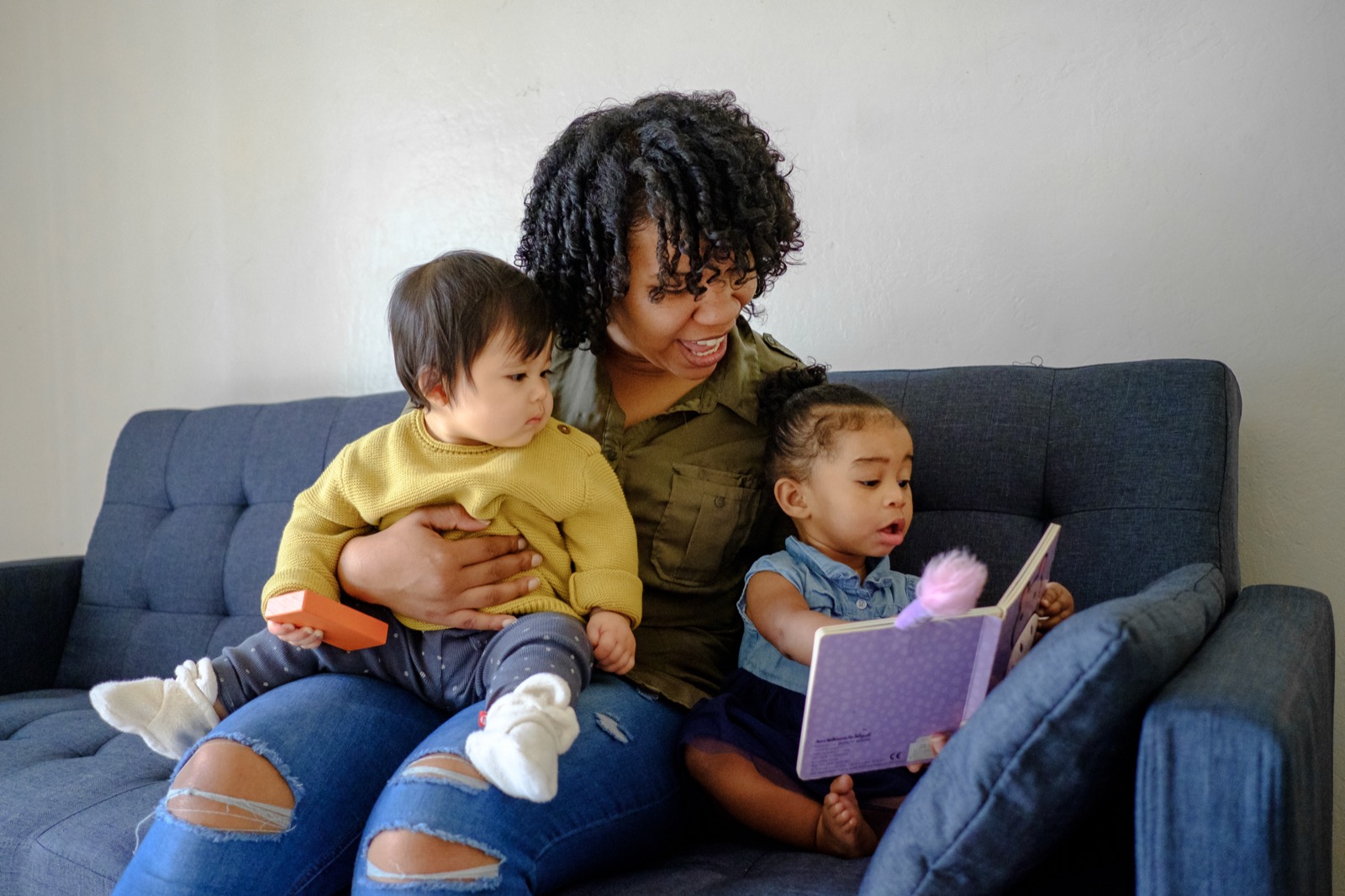 A provider reading a book with two toddlers on a couch