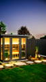 Backyard garden sauna with warm interior lighting and garden spike lights highlighting landscaping and pathway.